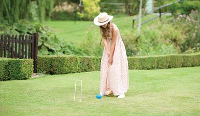 A woman in sun hat and summer dress playing croquet